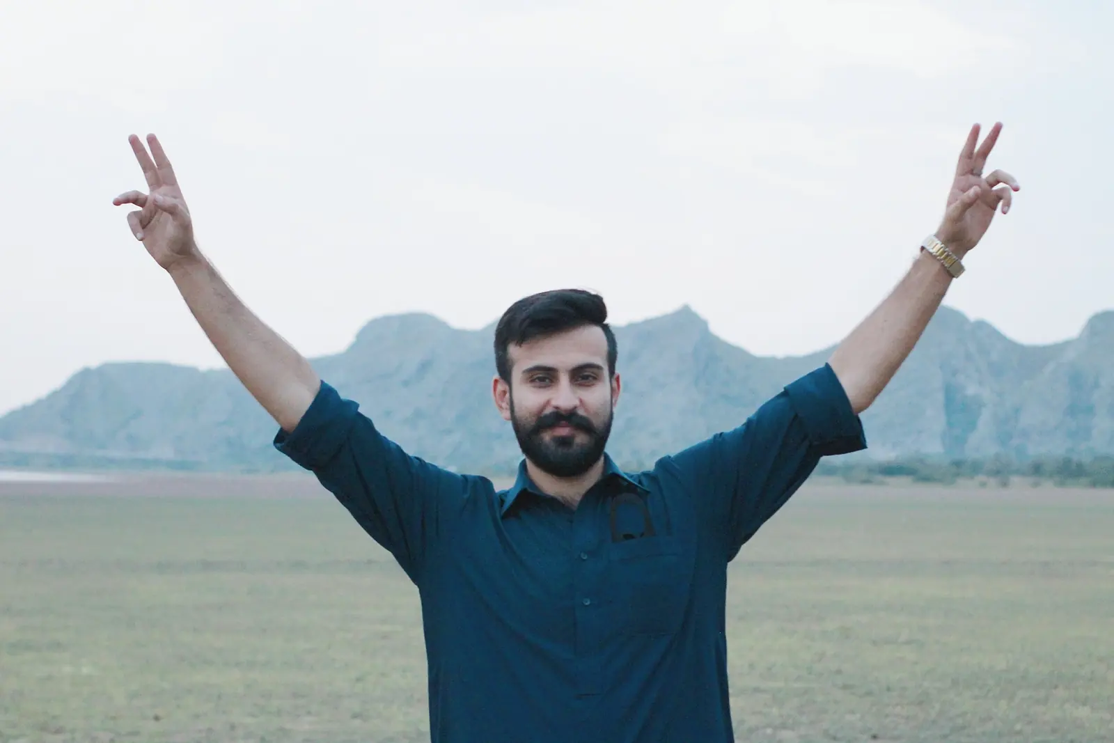 Salman Haider standing with arms raised in front of mountains